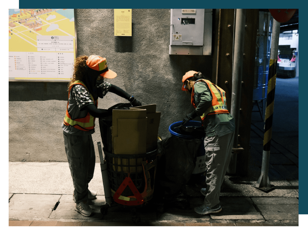 Two men in safety vests and hard hats loading a dumpster.